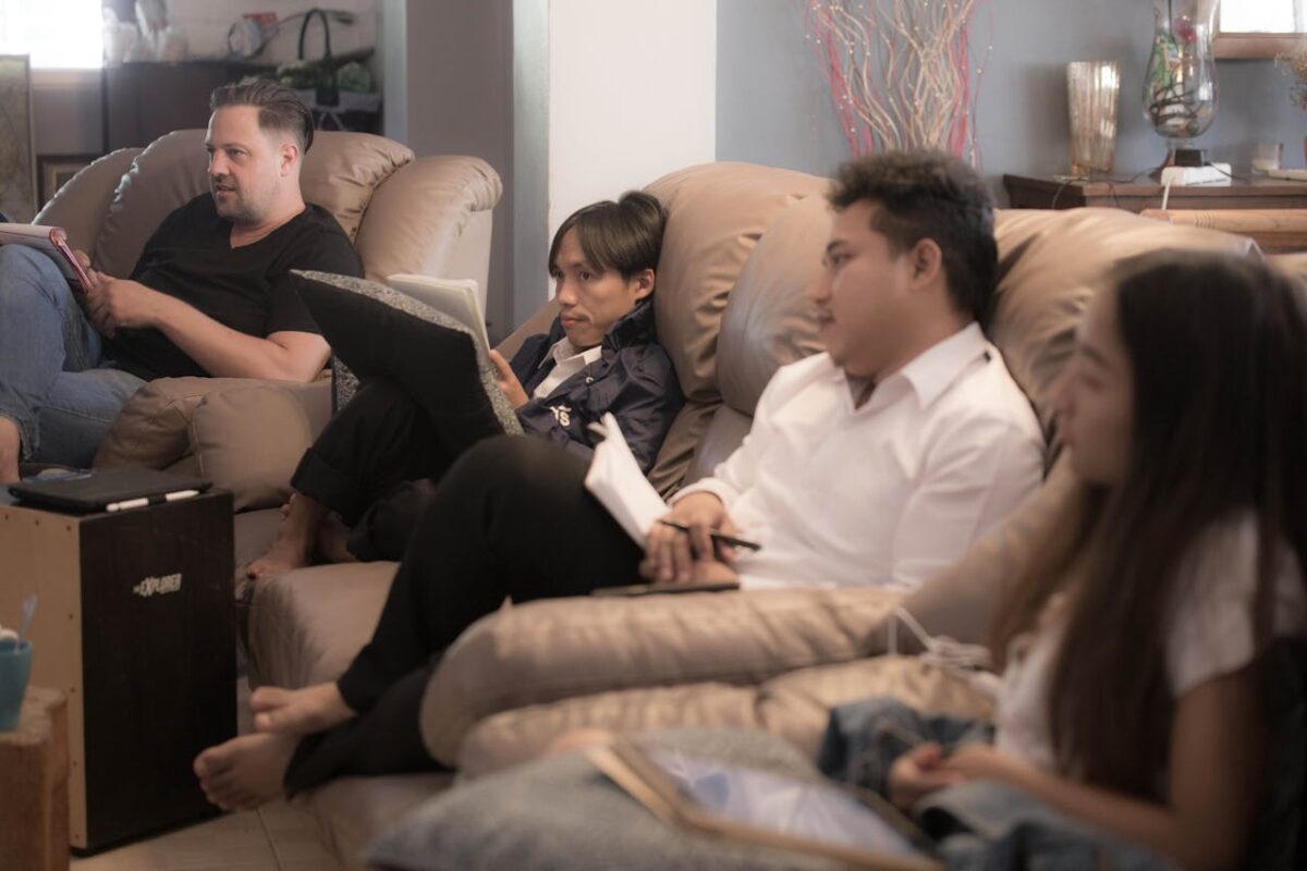 Services Four adults sitting on sofas indoors, actively engaged in discussion and writing.