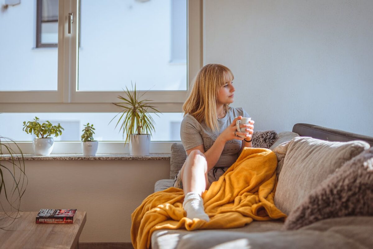 Woman enjoying a relaxing moment with coffee on a comfy sofa by the window.