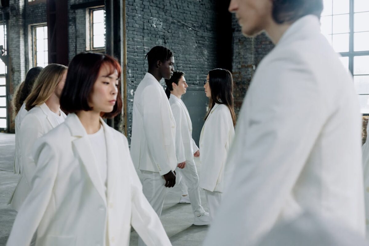 A group of diverse models in white suits walking indoors with natural light.