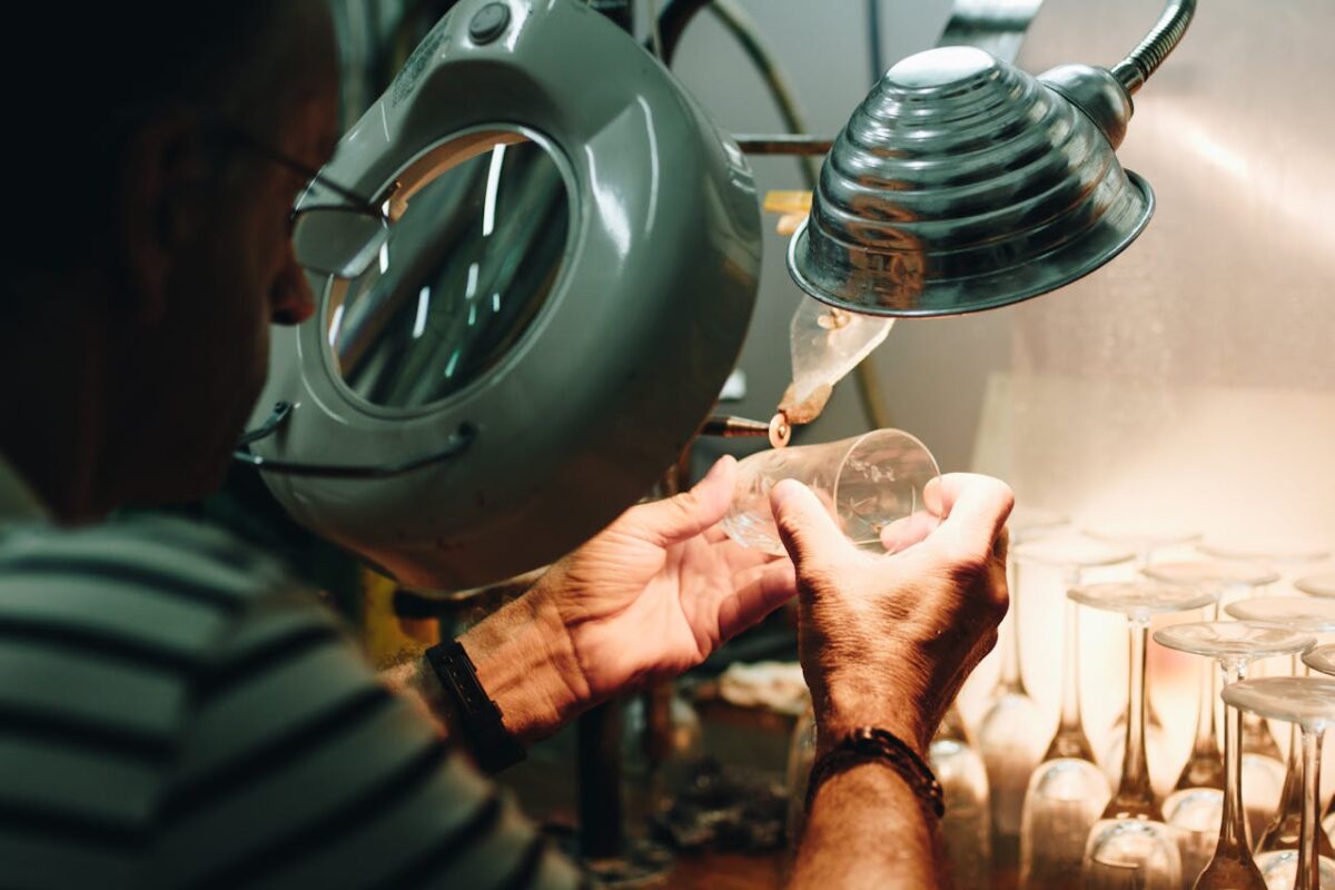 Services An artisan carefully shaping a glass piece under magnifying lamp indoors.