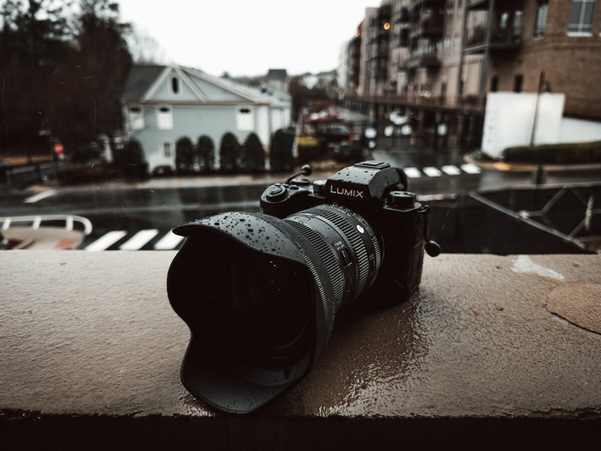 Services A Lumix camera sits on a wet balcony railing on a rainy day in the city.